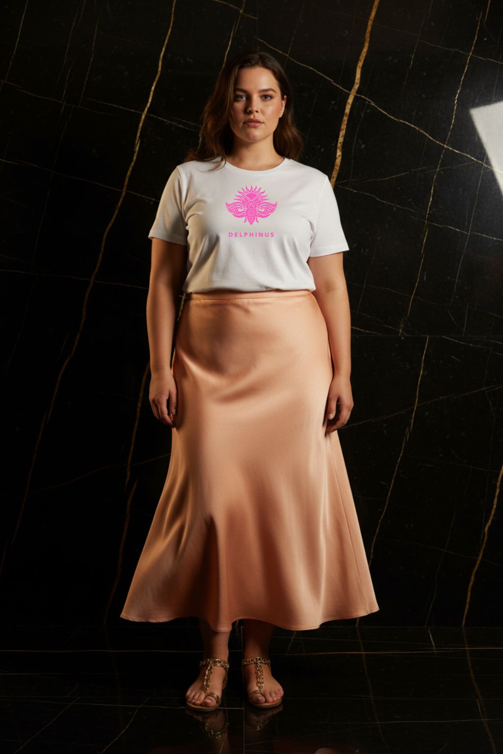 LA PÉTILLANTE CURVE – T-shirt unisexe blanc logo rose DELPHINUS, jeune femme curve naturelle, ambiance premium marbre noir et or, jupe fluide et sandales dorées, DELPHINUS