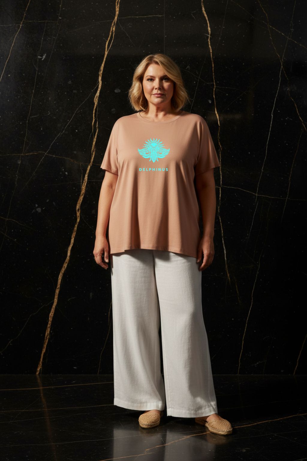 L'ÉVASION CURVE – T-shirt unisexe nude beige logo turquoise DELPHINUS, femme curve mature et élégante, ambiance premium marbre noir et or, pantalon large et espadrilles, DELPHINUS