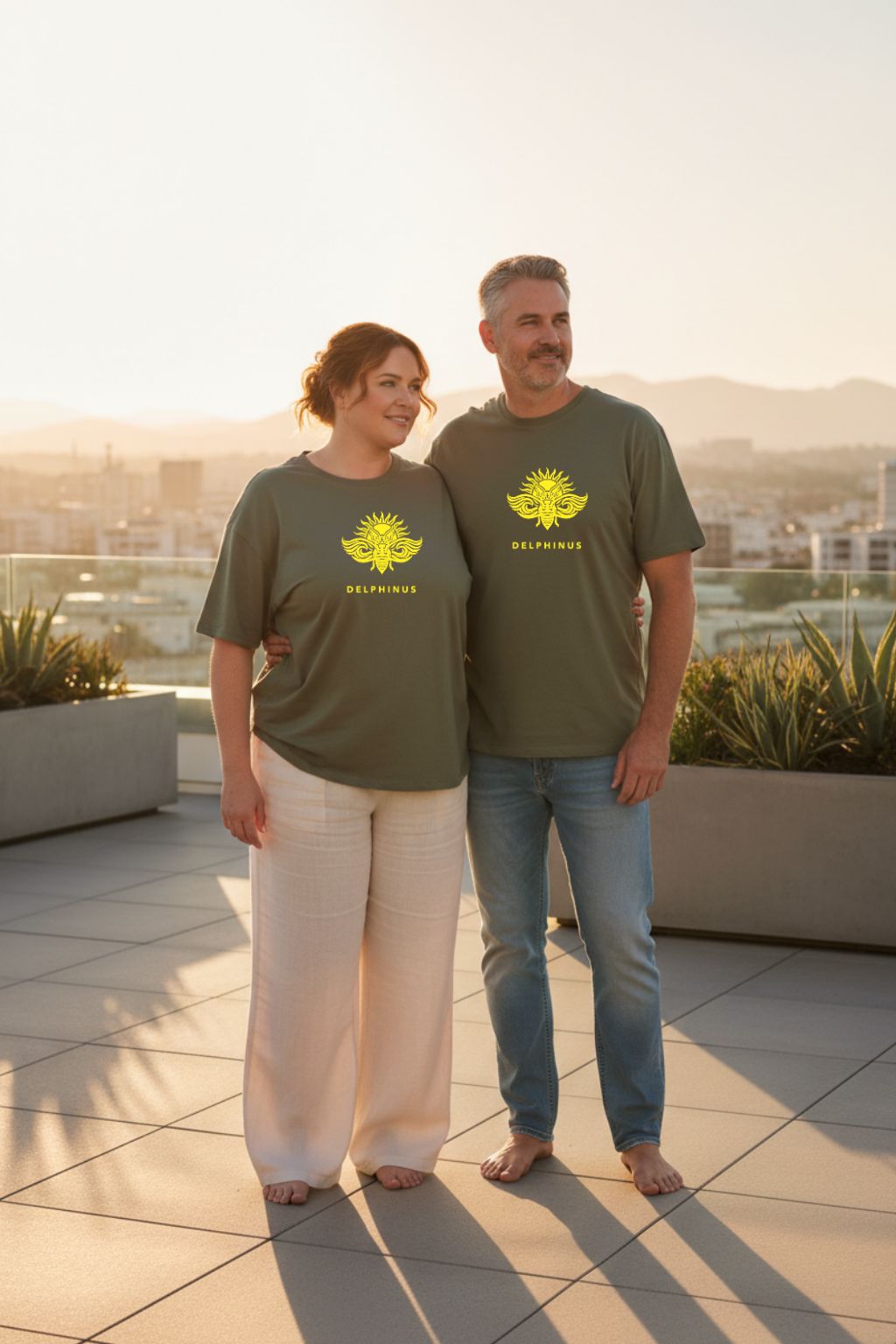 LE REBELLE CURVE – T-shirt unisexe kaki logo jaune DELPHINUS, couple curve élégant, rooftop coucher de soleil lumière dorée, pantalon crème et jean clair, DELPHINUS
