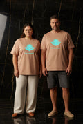 L'ÉVASION CURVE – T-shirt unisexe nude beige logo turquoise DELPHINUS, couple curve élégant, ambiance premium marbre noir et or, tenues estivales modernes, DELPHINUS