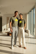 LE REBELLE – T-shirt unisexe kaki logo jaune DELPHINUS, couple jeune et élégant, intérieur luxueux lumière dorée, tenues estivales modernes, DELPHINUS
