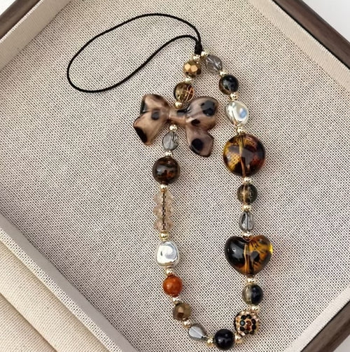 Bijou de téléphone – perles brunes, nacrées et dorées avec nœud et cœur effet écaille, DELPHINUS