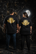 LE SIGNATURE CURVE – T-shirt unisexe oversize noir logo cigale doré, couple curve de dos, ambiance luxe marbre noir et or, DELPHINUS