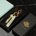 Écrin Cadeau DELPHINUS avec bijou de sac — boîte noire mate logo or cigale, accessoire de sac présenté dans son coffret, ambiance noir et or dramatique
