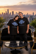 LA LIBERTÉ DELPHINUS – T-shirt unisexe Curve Noir & logo bleu, duo homme et femme 50 ans corpulence généreuse, rooftop coucher de soleil, mise en scène premium
