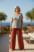 LA PERLE GRISE CURVE – Femme très curve 50 ans en palazzo terracotta et t-shirt gris col V logo cigale, terrasse rooftop vue mer, DELPHINUS